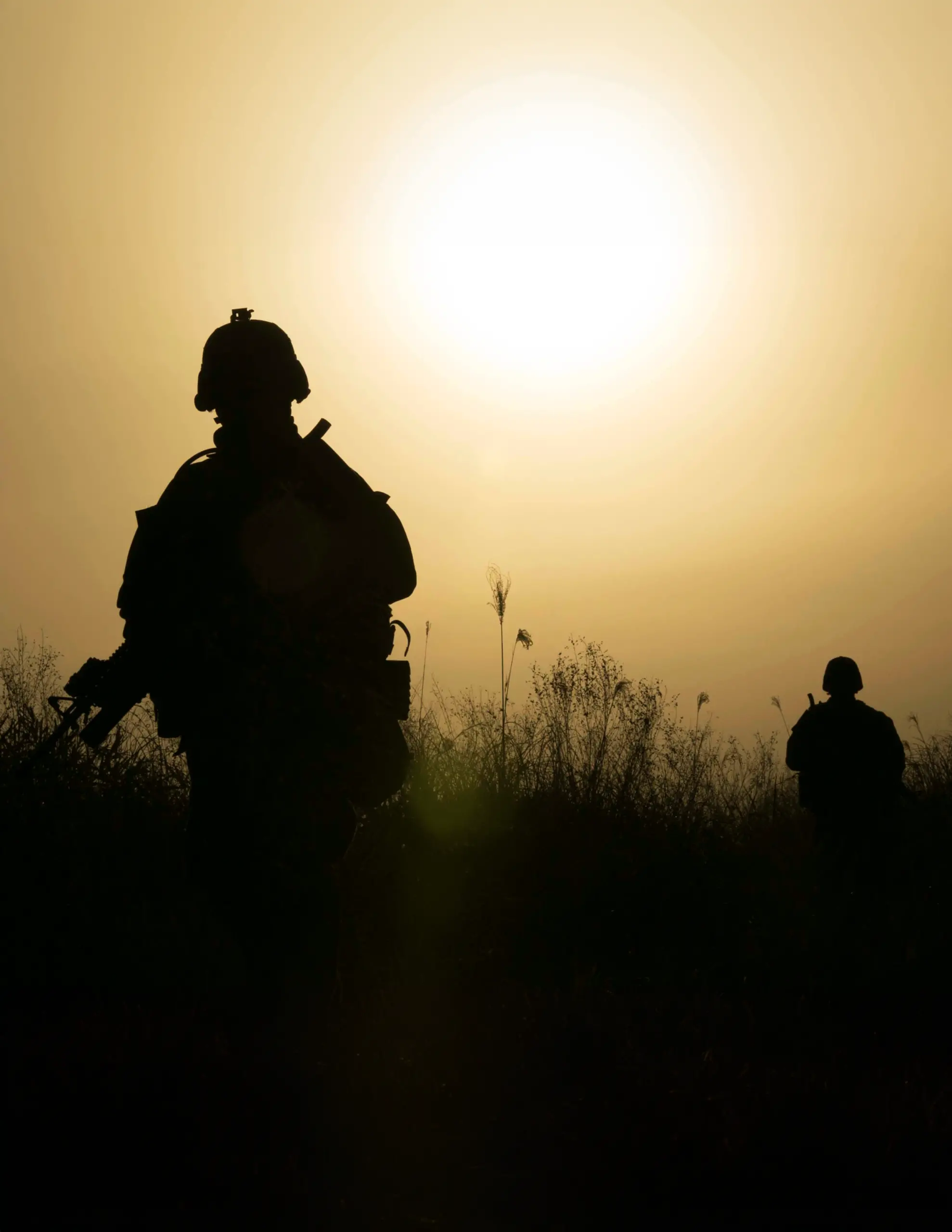 Image of a silhouette of two soldiers with the sun setting.